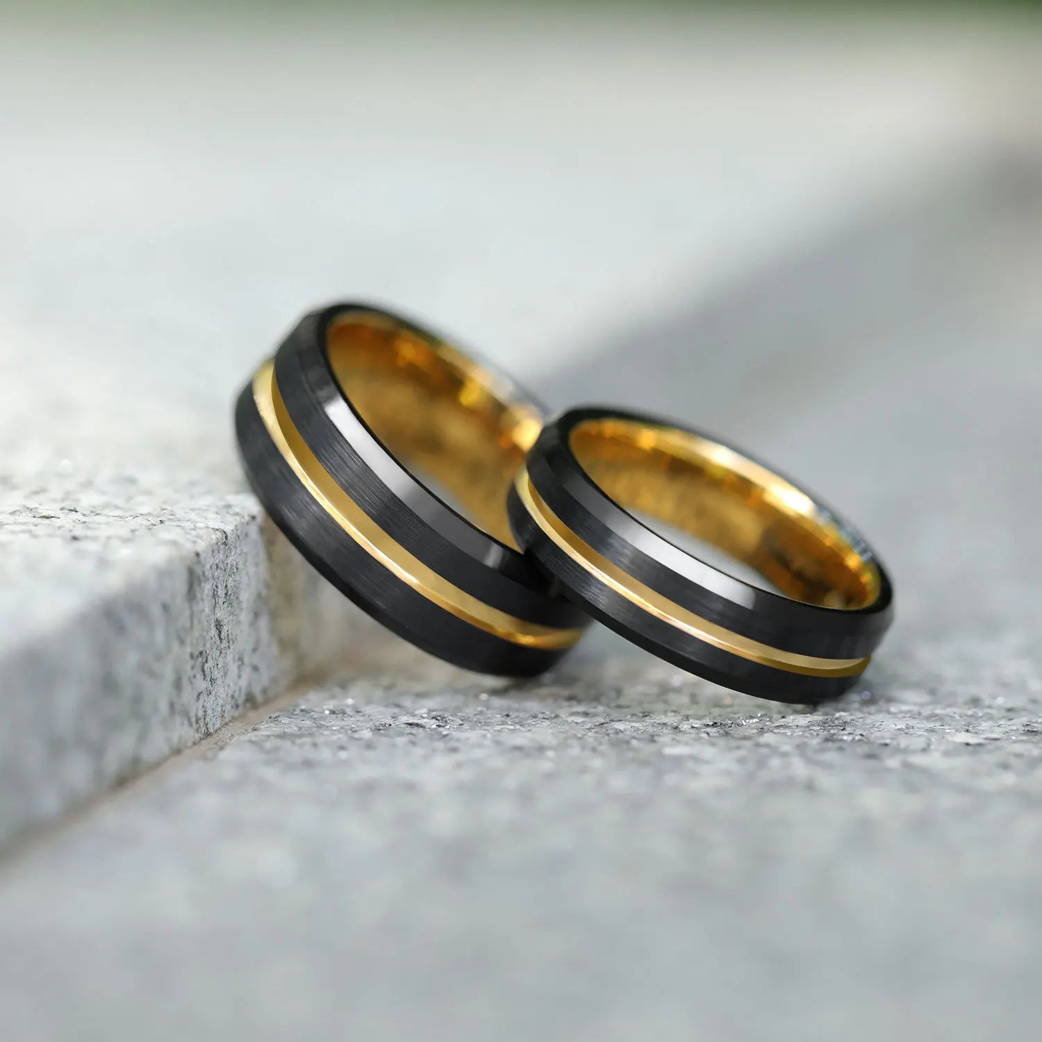 Set of 8mm and 6mm black Tungsten rings featuring brushed exteriors, polished gold interiors, and gold stripes for a bold, matching look.