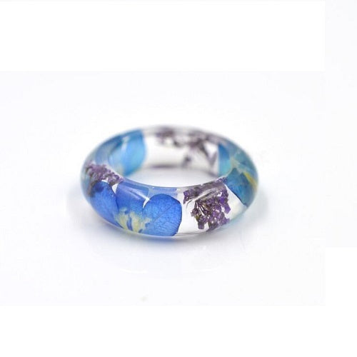 Clear botanical resin ring with tiny preserved wildflowers visible around the band.