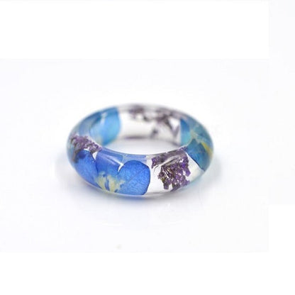 Clear botanical resin ring with tiny preserved wildflowers visible around the band.