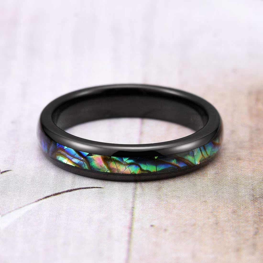 Elegant black Tungsten ring featuring a vibrant abalone shell inlay against a soft background.