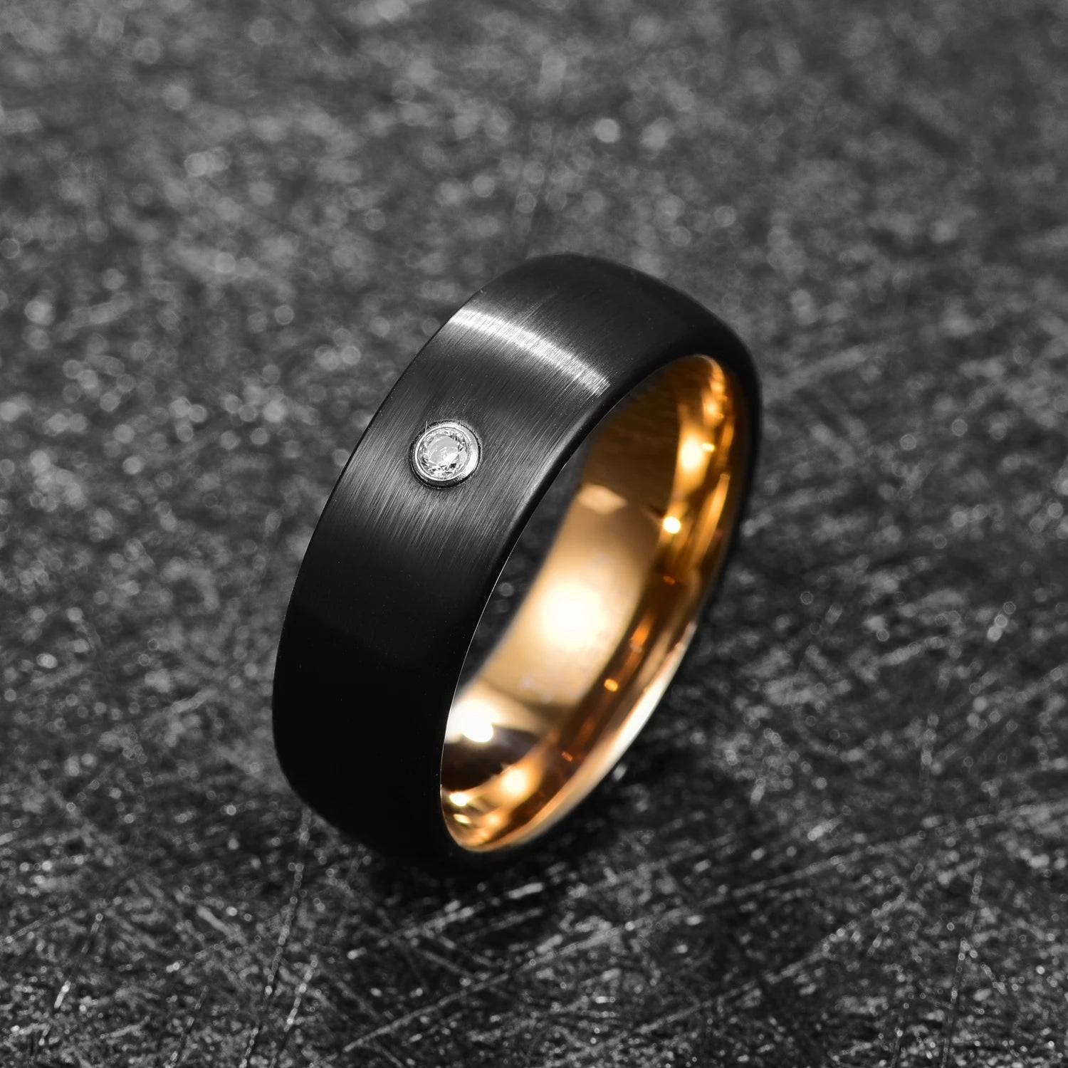 Angled view of gold and black Tungsten men’s ring with flush-set cubic zirconia stone, showing brushed black exterior and gold interior