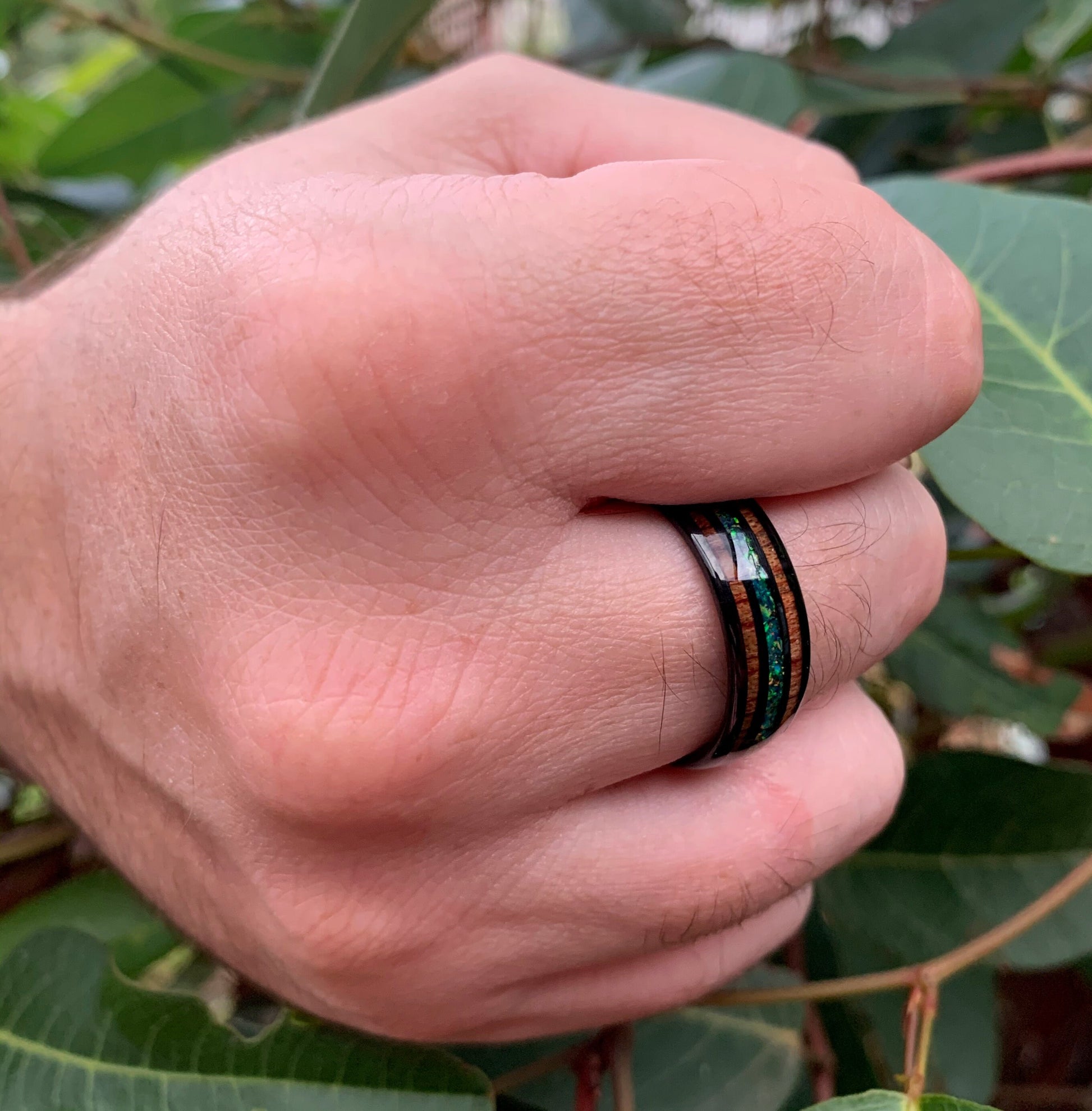 Men's hand wearing a tungsten ring with acacia wood and green opal inlay, showcasing the ring's comfort fit and design.