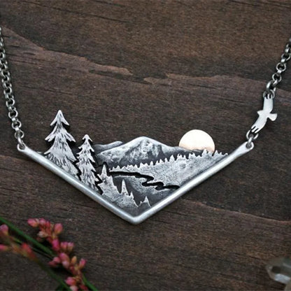 Mountain necklace featuring a detailed silver landscape with pine trees.