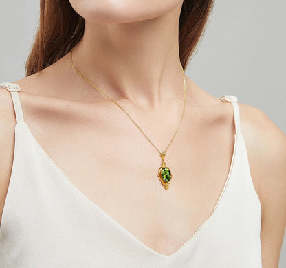 Ornate yellow gold peridot pendant with a luminous green oval gemstone worn around a woman's neck.