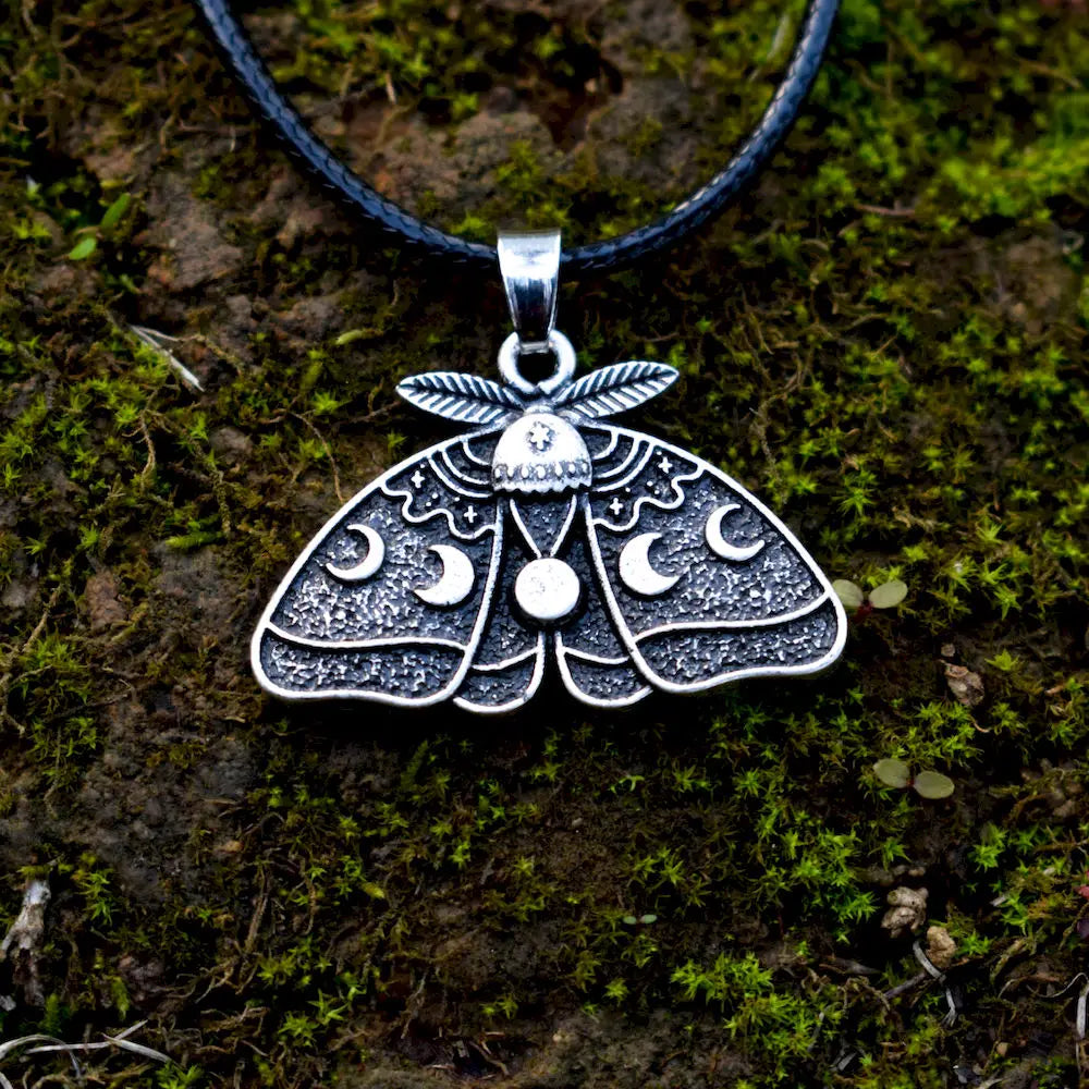 Silver-toned moth design with symbolic waxing and waning moons, hanging on a black necklace cord.