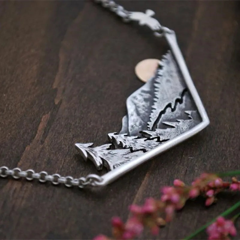 Silver pendant with pine trees, rugged peaks and a setting sun.