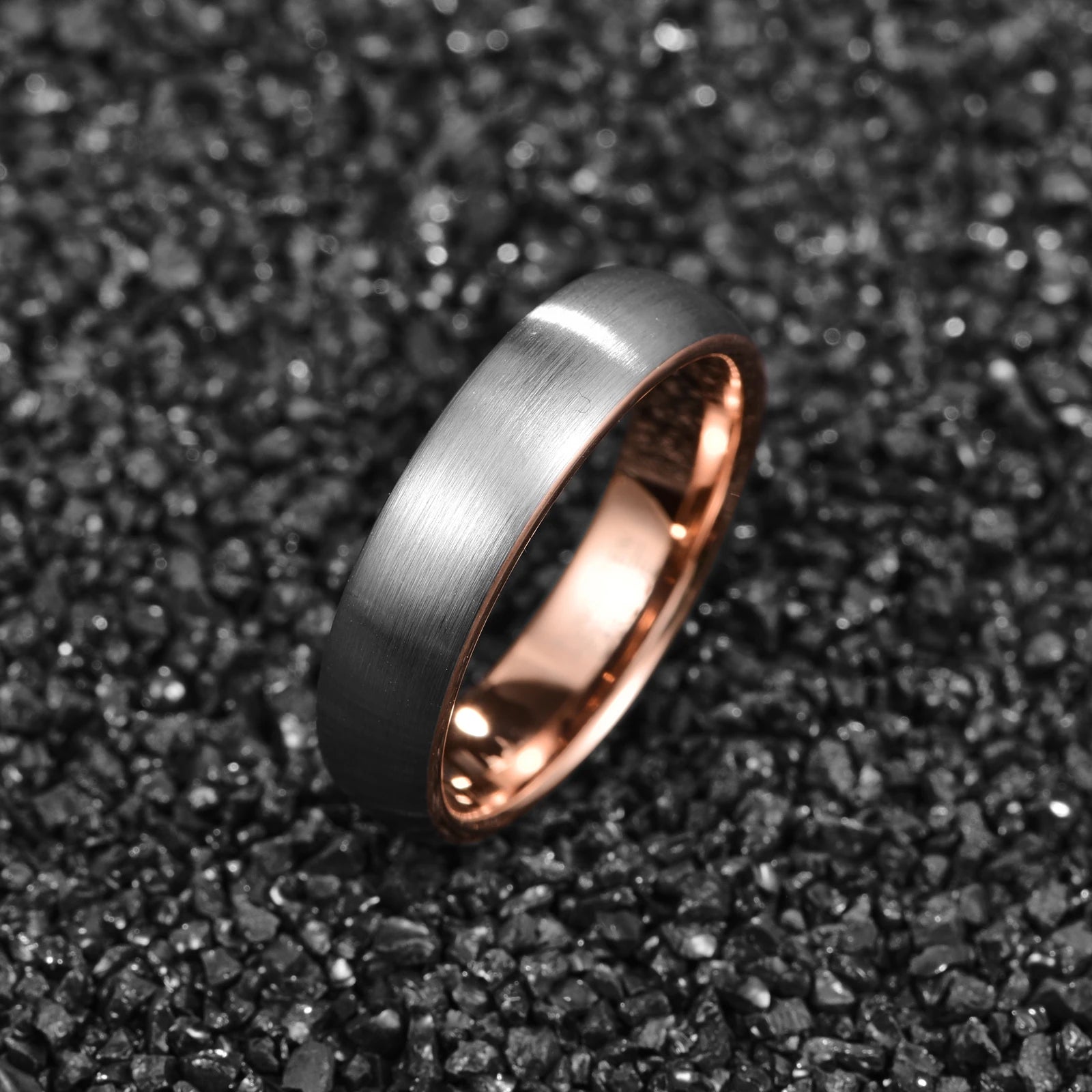 Unisex domed Tungsten ring with a brushed silver outer band and smooth rose gold inner band, displayed on a black textured surface.