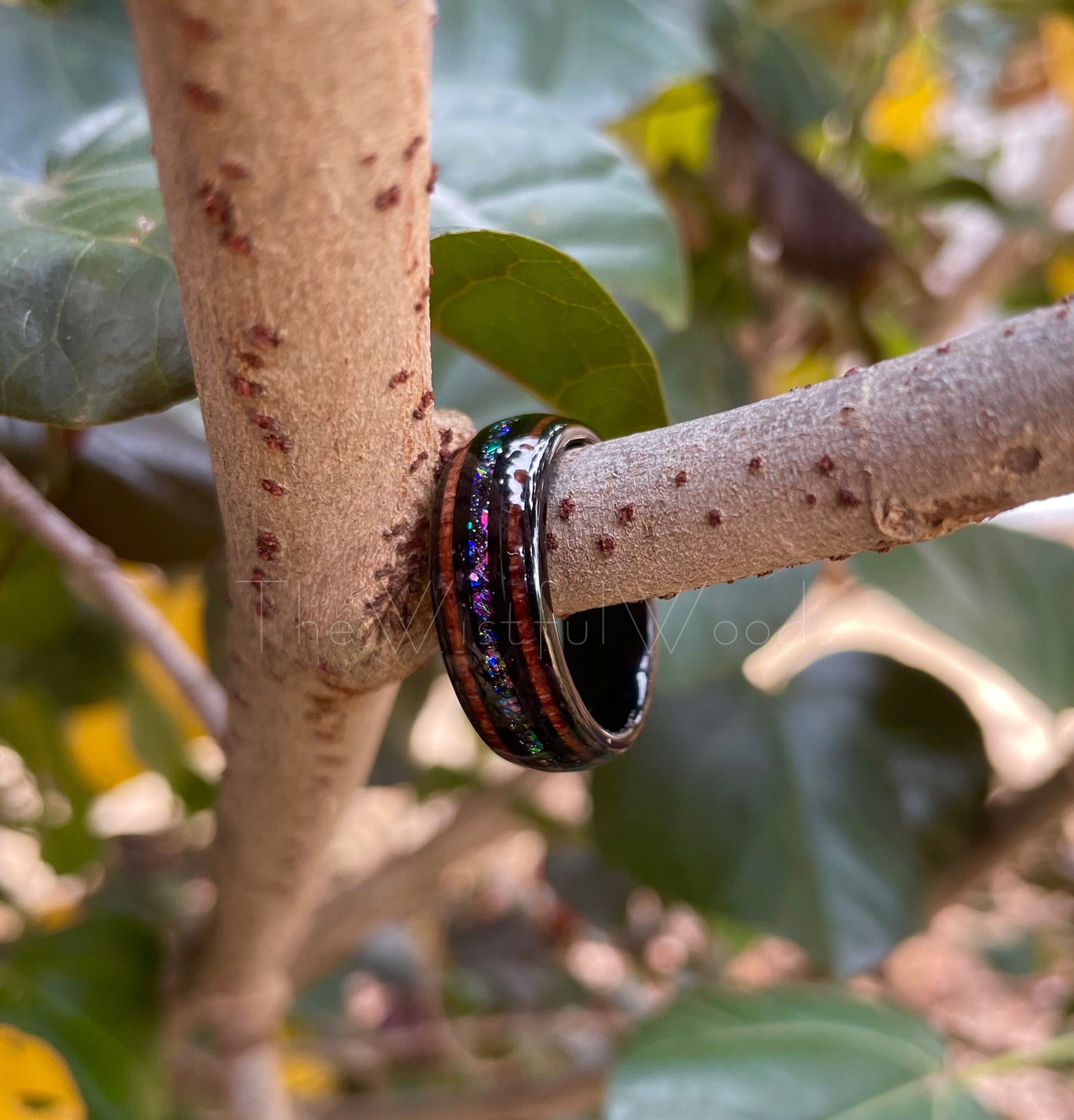 8mm Tungsten supernova ring with galaxy inlay featuring real Moon dust, holographic flakes, opal chunks, and acacia wood, resting on a branch.