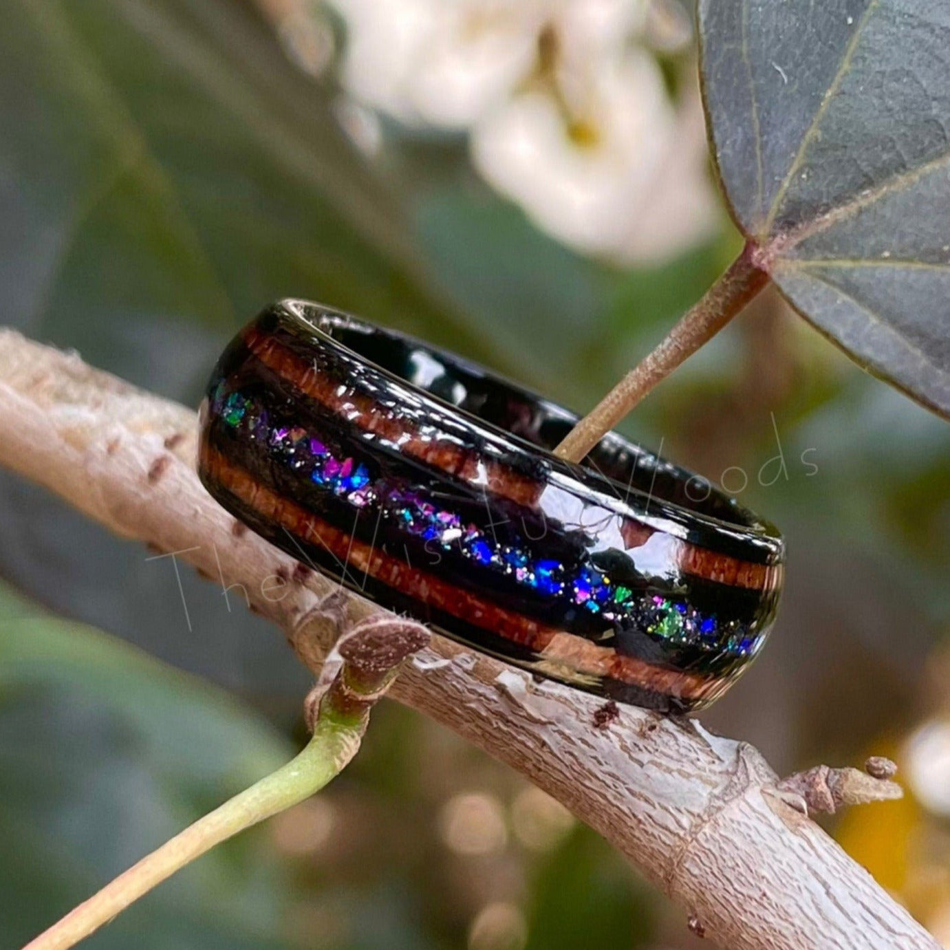 Iridescent supernova Tungsten ring with Moon dust, acacia wood, holographic flakes, and crushed opal inlay, resting on a branch.