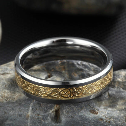 Celtic dragon wedding band with gold inlay on silver Tungsten, resting on stone.