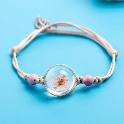 Nature-inspired cord bracelet with a preserved botanical centerpiece and delicate bead details.