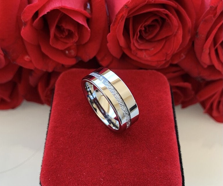 Polished silver Tungsten men's ring with Gibeon meteorite inlay, displayed on a red velvet background with roses.