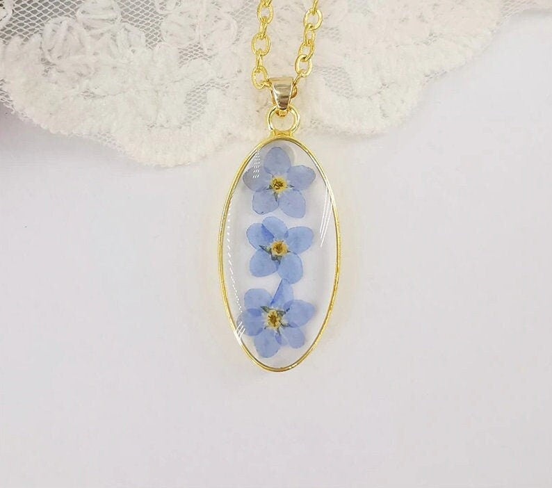 Pressed flower jewelry featuring three forget-me-nots preserved in a gold pendant.