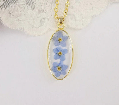 Pressed flower jewelry featuring three forget-me-nots preserved in a gold pendant.