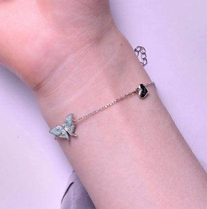 Side view showing the pale green moth centerpiece and a dangling silver heart charm.