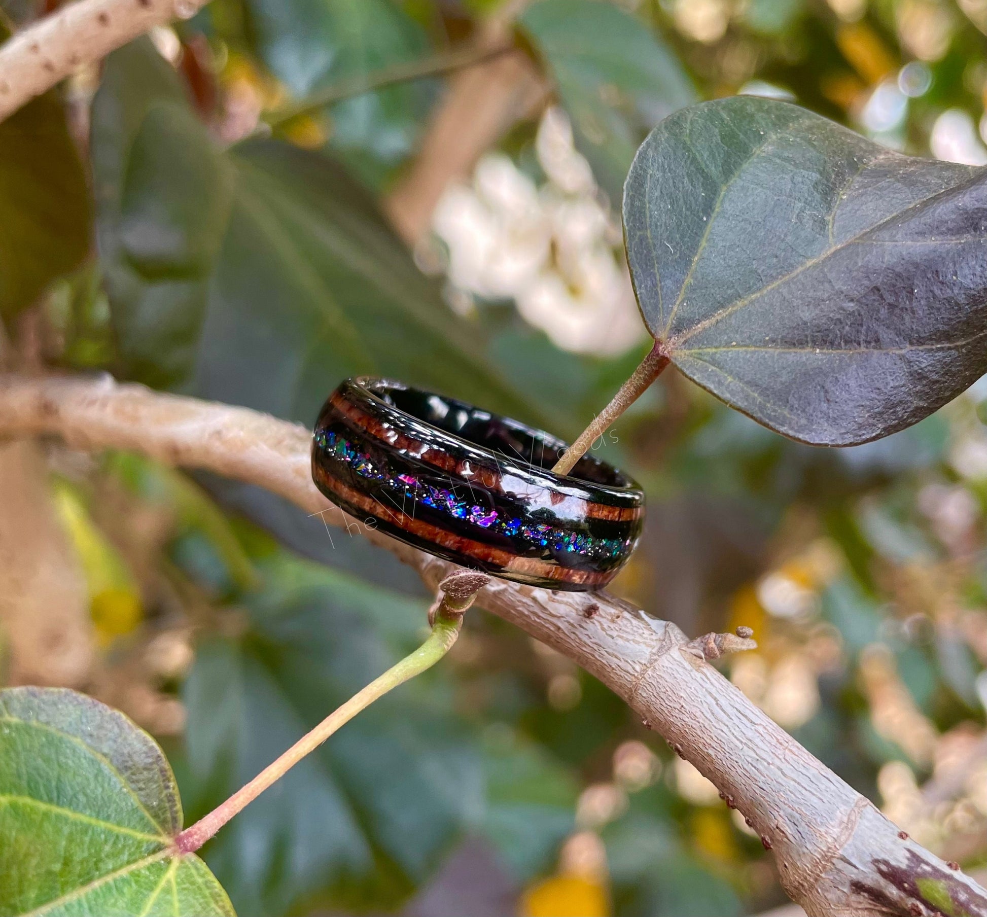 Supernova black Tungsten ring with holographic flakes, crushed opal, Moon dust, and acacia wood inlay, placed on a tree branch.