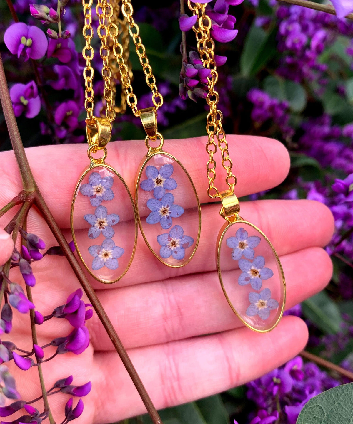 Three oval floral pendants displayed side by side, containing delicate blue forget-me-not flowers.