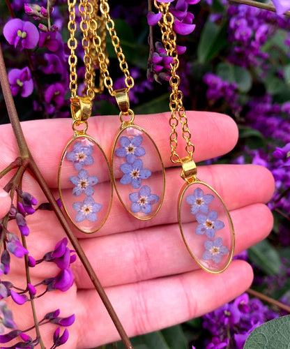Three oval floral pendants displayed side by side, containing delicate blue forget-me-not flowers.