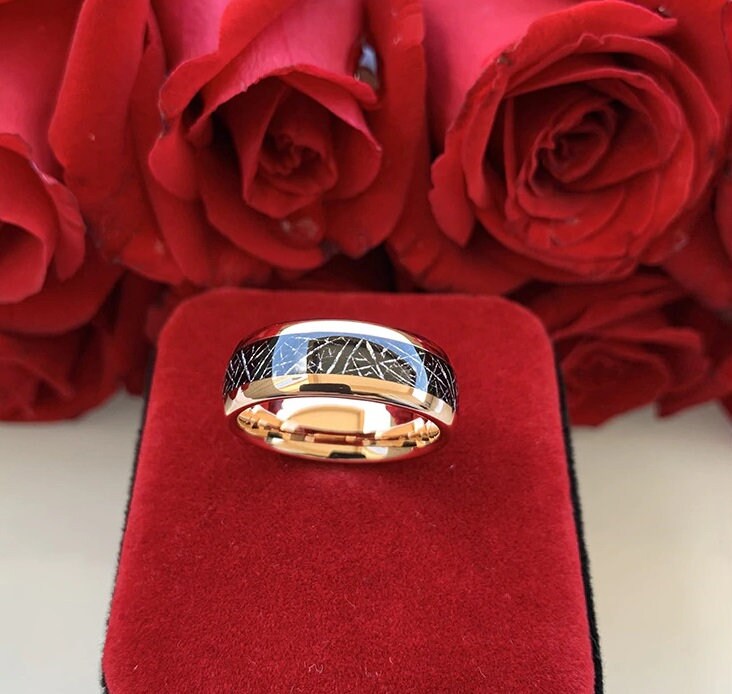 Tungsten and meteorite ring shown on a red velvet display with roses in the background.