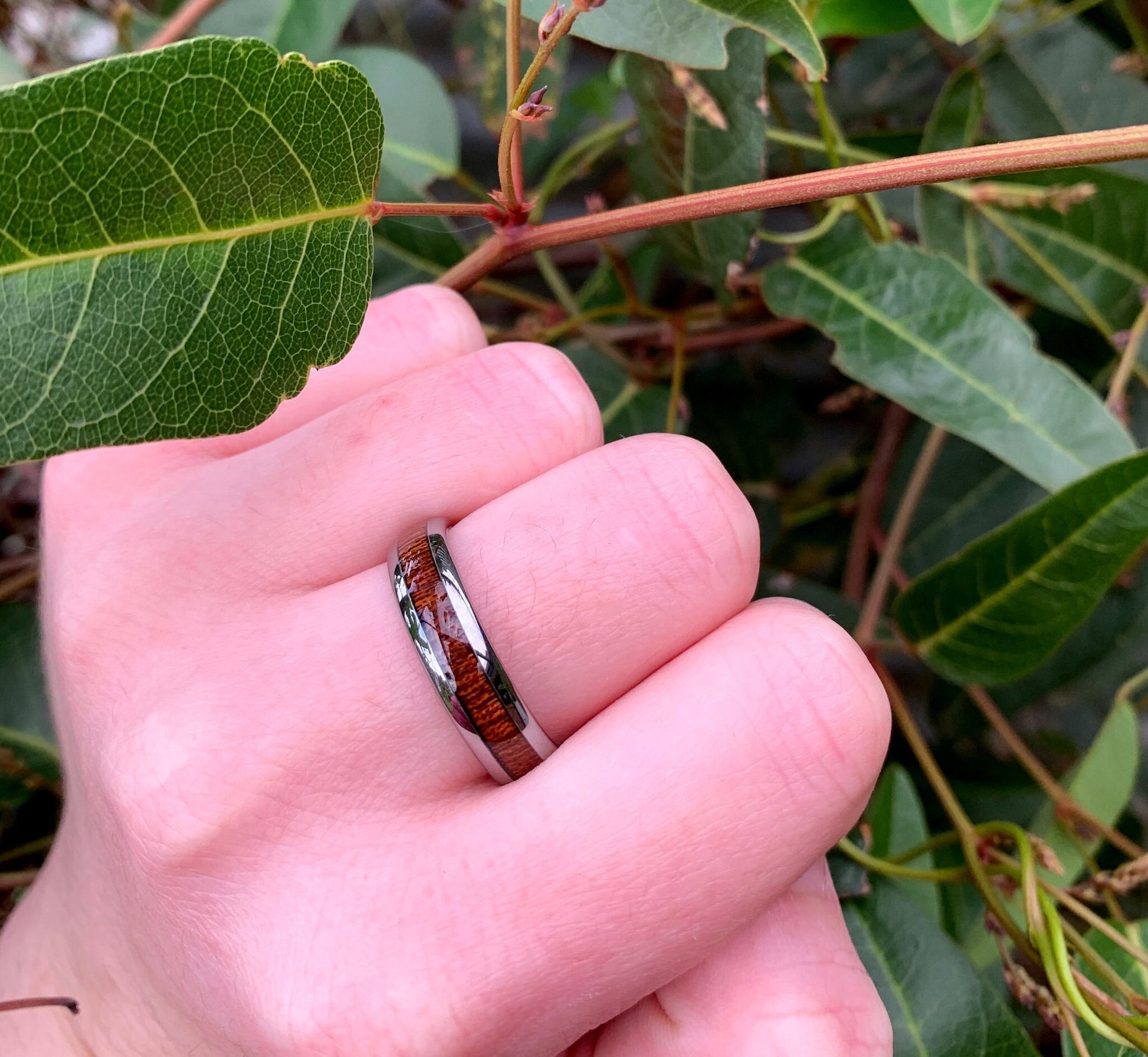 Silver Tungsten koa wood wedding bands on hand, showing the domed design and comfort fit.