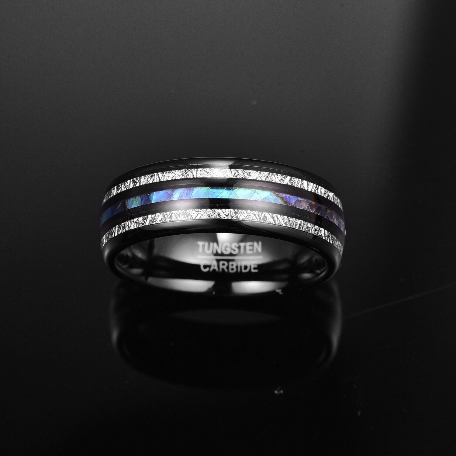 Tungsten ring with Gibeon meteorite and abalone shell inlays, showcased on a black reflective surface.